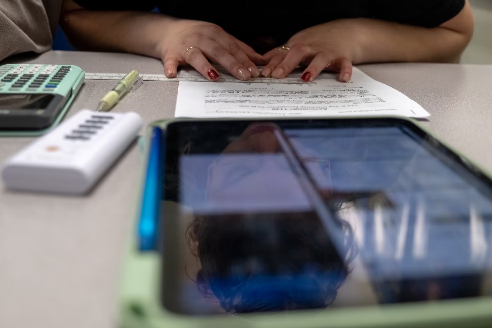 Hands on a table covering a paper. A tablet sits on the table at the foreground.