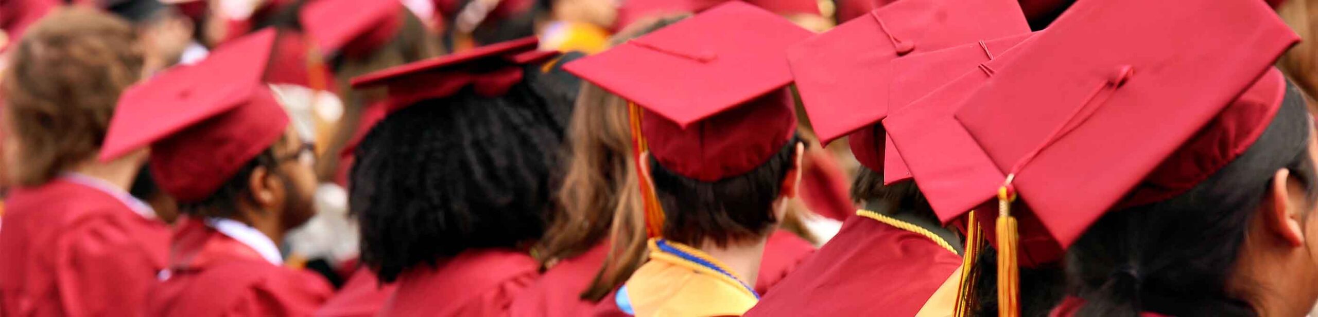 Students sit at graduation with their graduation caps facing the camera. 