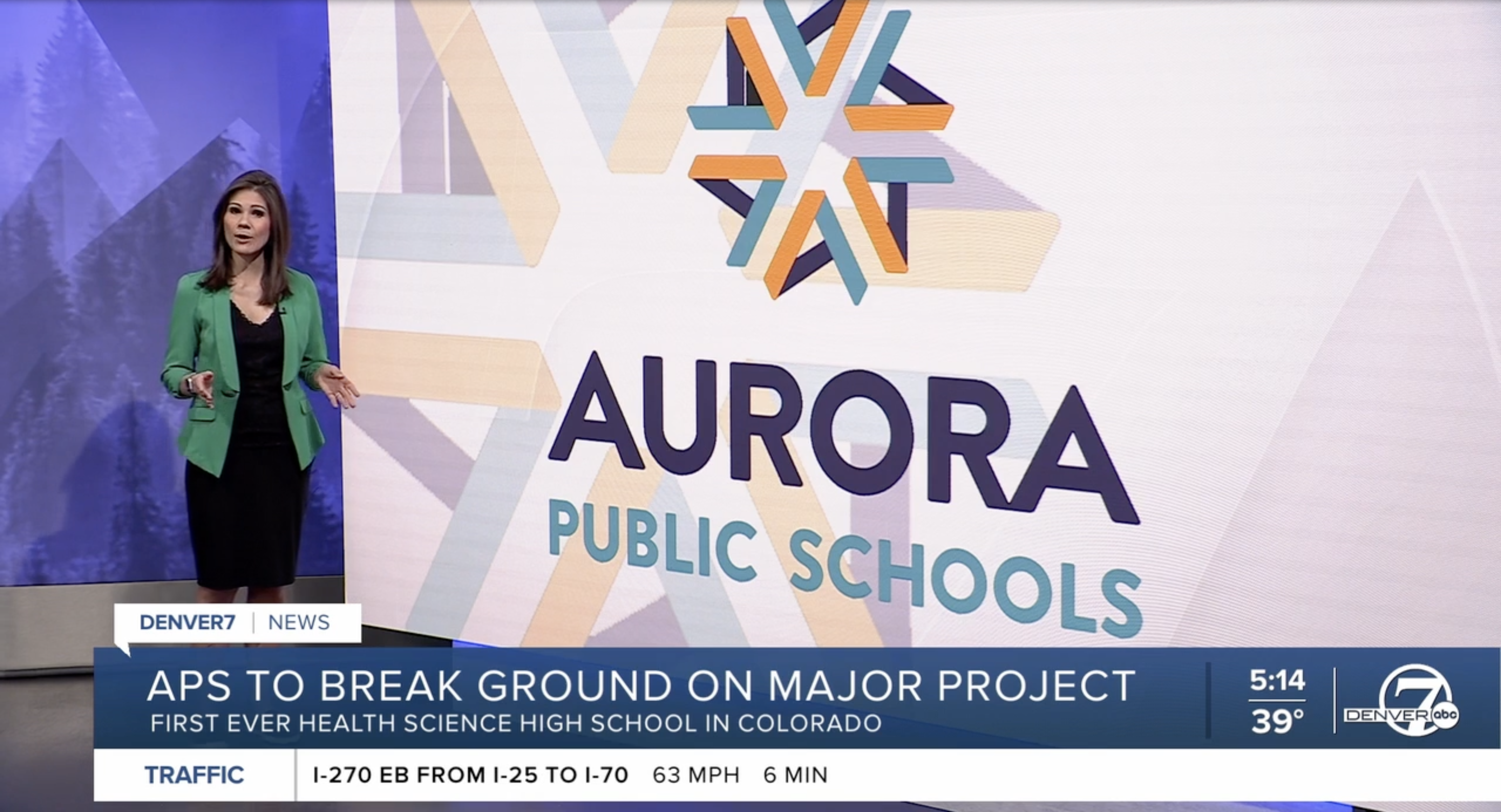 TV anchor stands in front of monitor that says Aurora Public Schools.