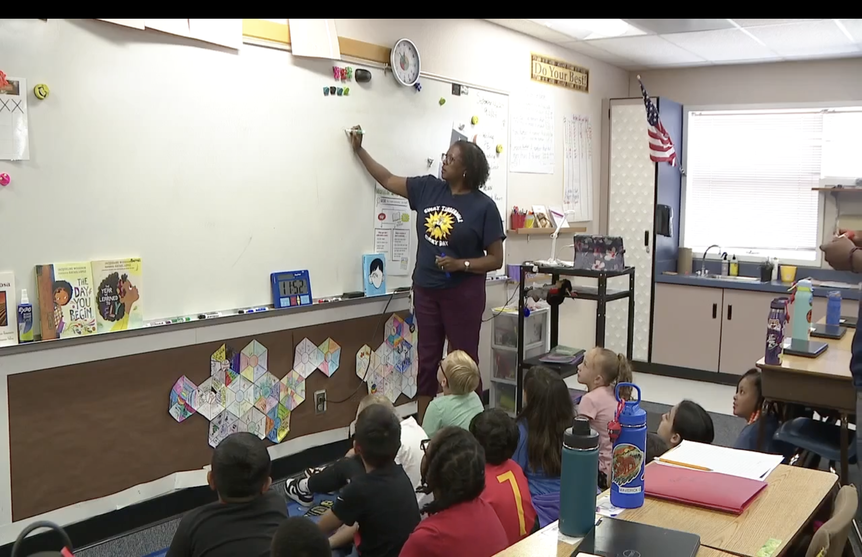 Teacher stands at front of class in front of students.