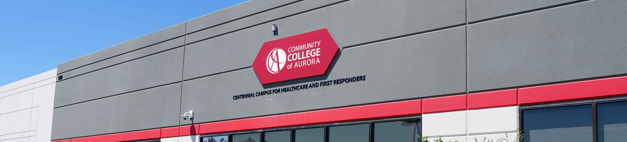 Photo of gray building with a red sign for the Community College of Aurora Centennial Campus for Healthcare and First Responders.