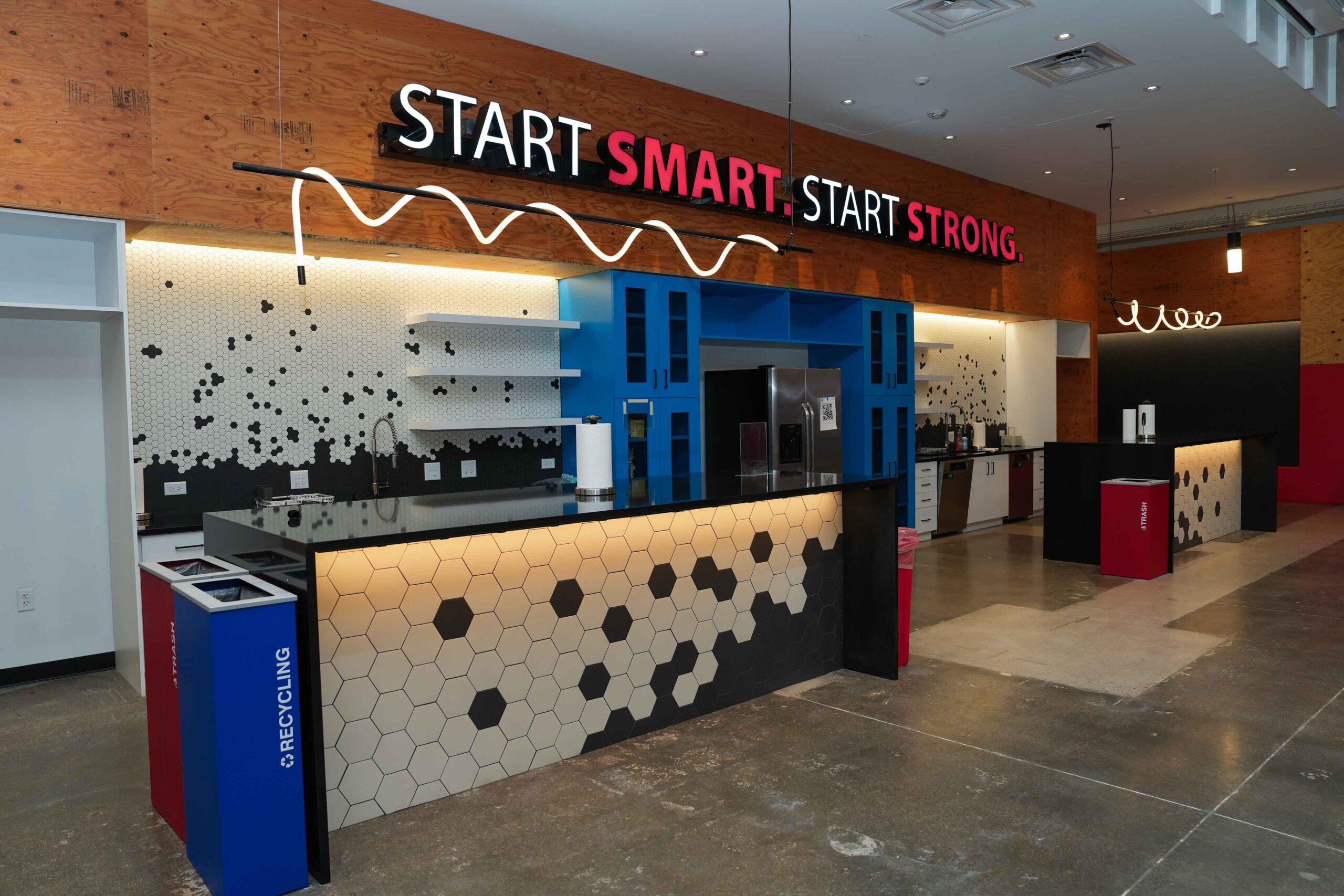 Modern interior with glossy floor, hexagonal black-and-white counter, and blue shelving. Red and black signs read 'Start Smart, Start Strong.'