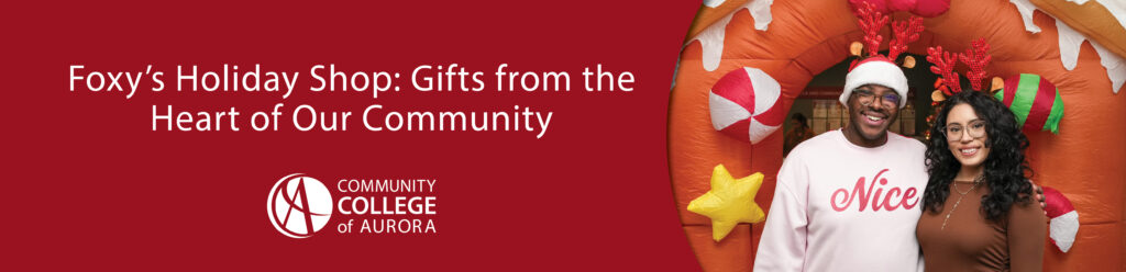 Two smiling people wearing reindeer antlers stand in front of an inflatable gingerbread house decorated with candy. One wears a Santa hat and a sweatshirt that says “Nice.” Below the photo, text reads, “Foxy’s Holiday Shop: Gifts from the Heart of Our Community,” with the Community College of Aurora logo.