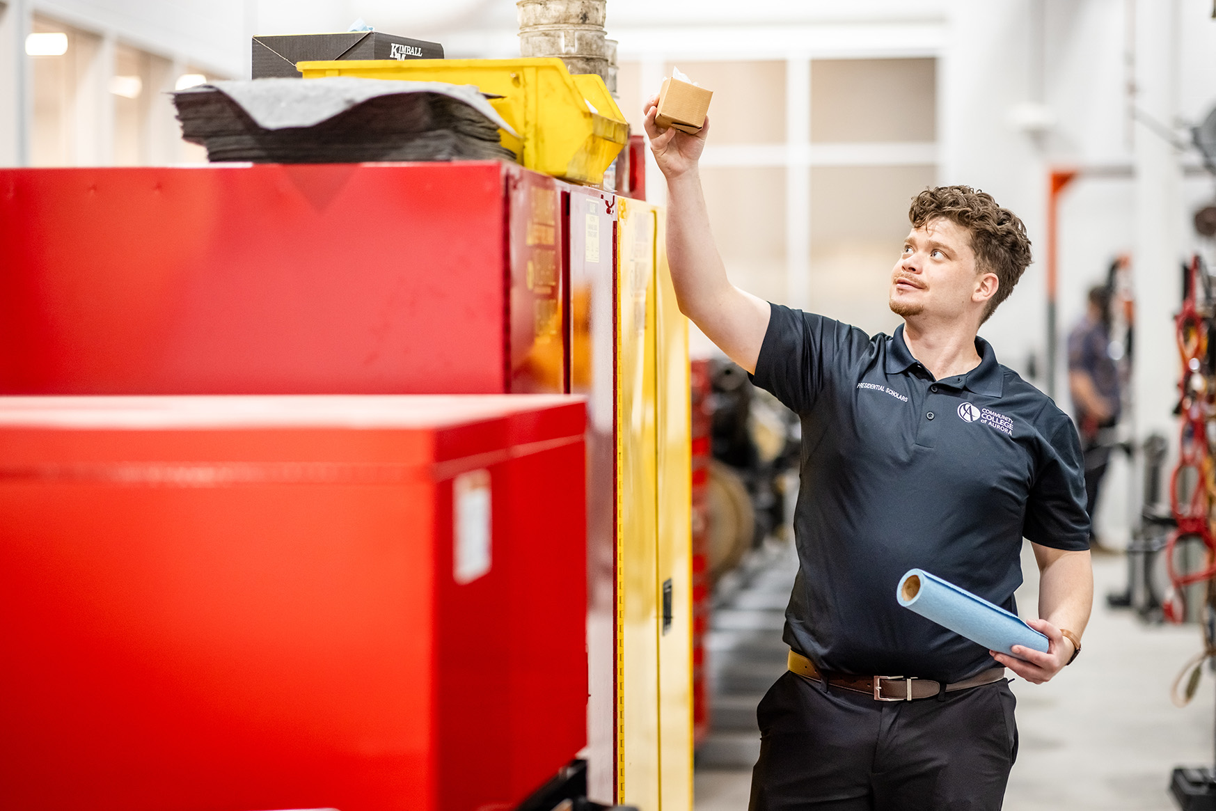 Photo of a person in a warehouse reaching up to grab an box from a red metal cabinet.