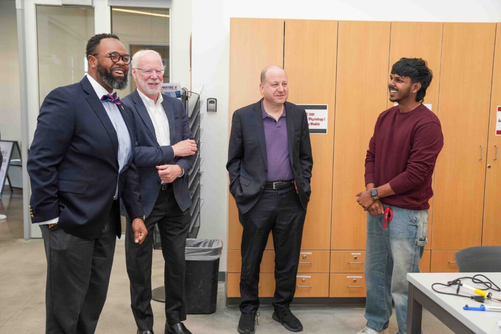 Four smiling men stand in a workshop. The atmosphere is professional and light.