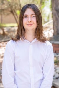 Portrait of Connor Ross standing outdoors, wearing a white button-down shirt and smiling at the camera.
