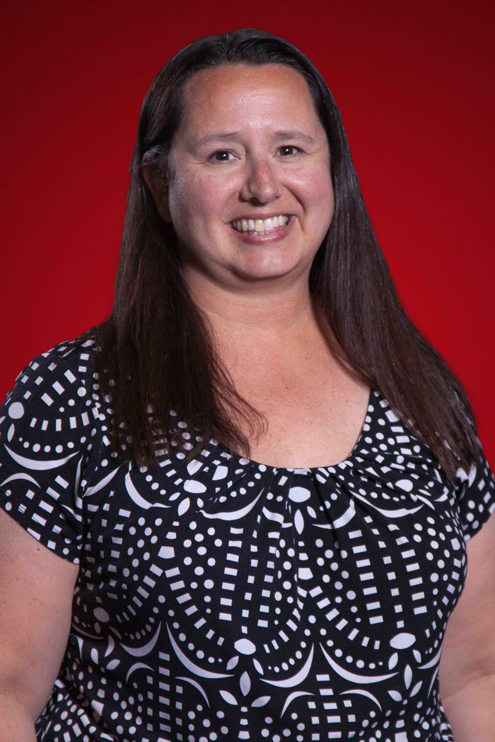 Photo of Dr. Mandy Geddes smiling on a red background.