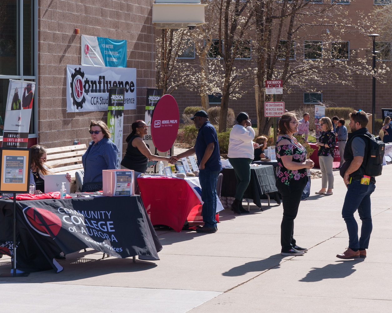 Students and employers talk at career fair booths outside on a college campus, with the Community College of Aurora Career Services table in the foreground.